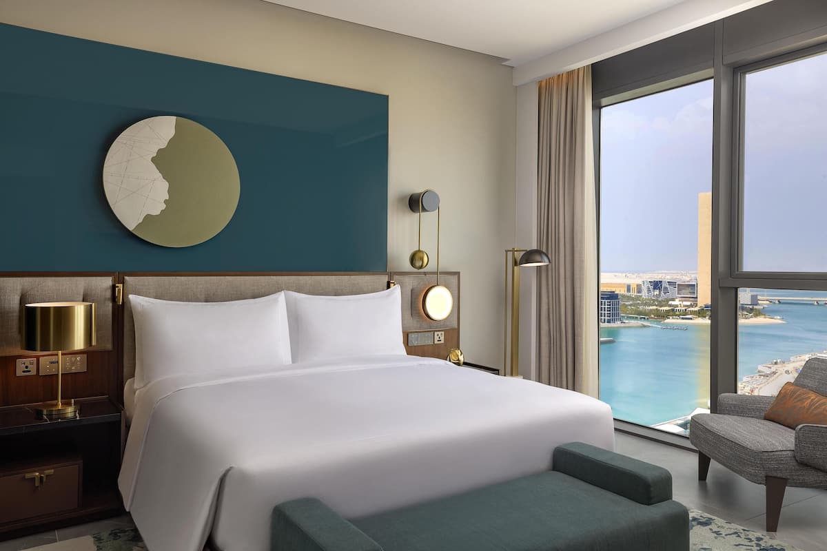 A hotel room with a large bed, a view of the sea, a round wall decoration, and a modern lamp.