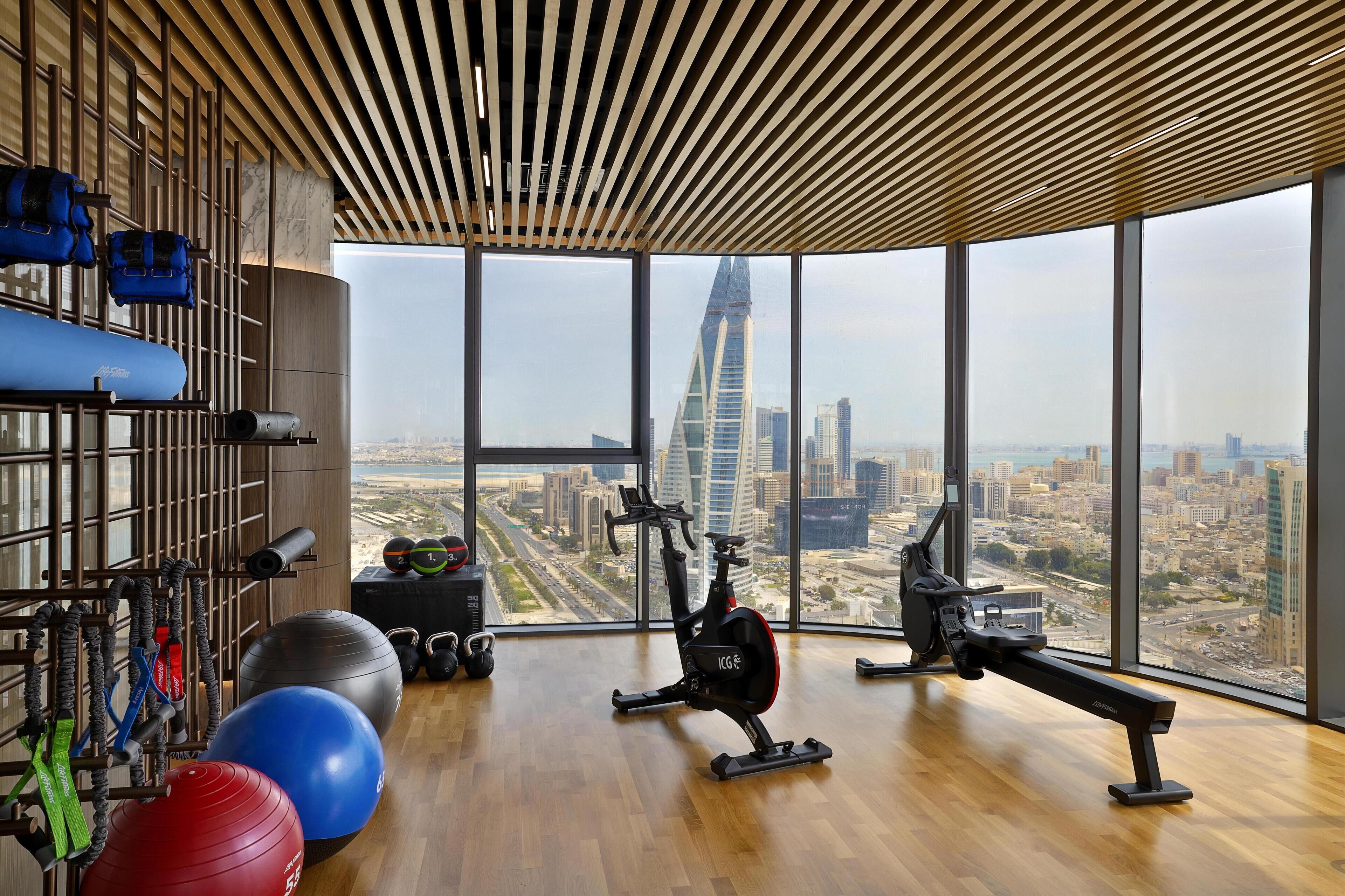 A gym with exercise equipment, large windows, and a city view.
