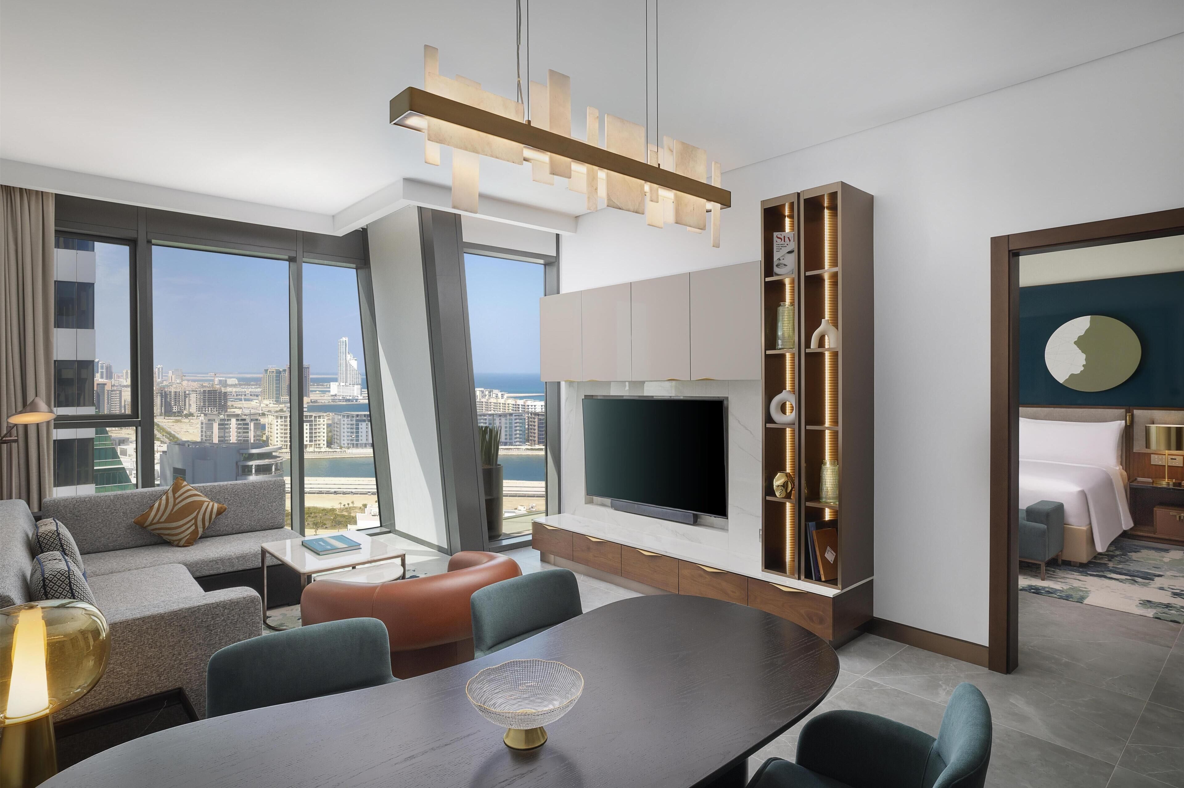A modern hotel room with a large TV, seating area, and a view of the city.