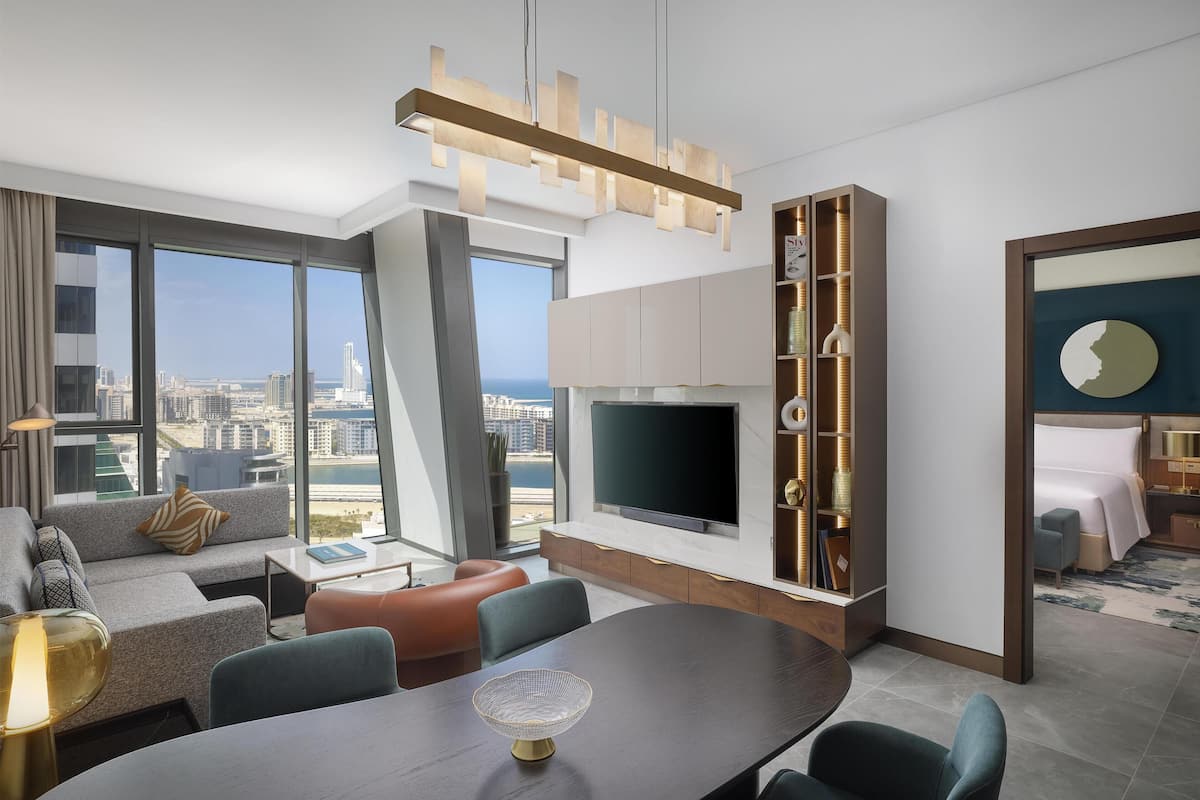 A modern hotel room with a large TV, seating area, and a view of the city.