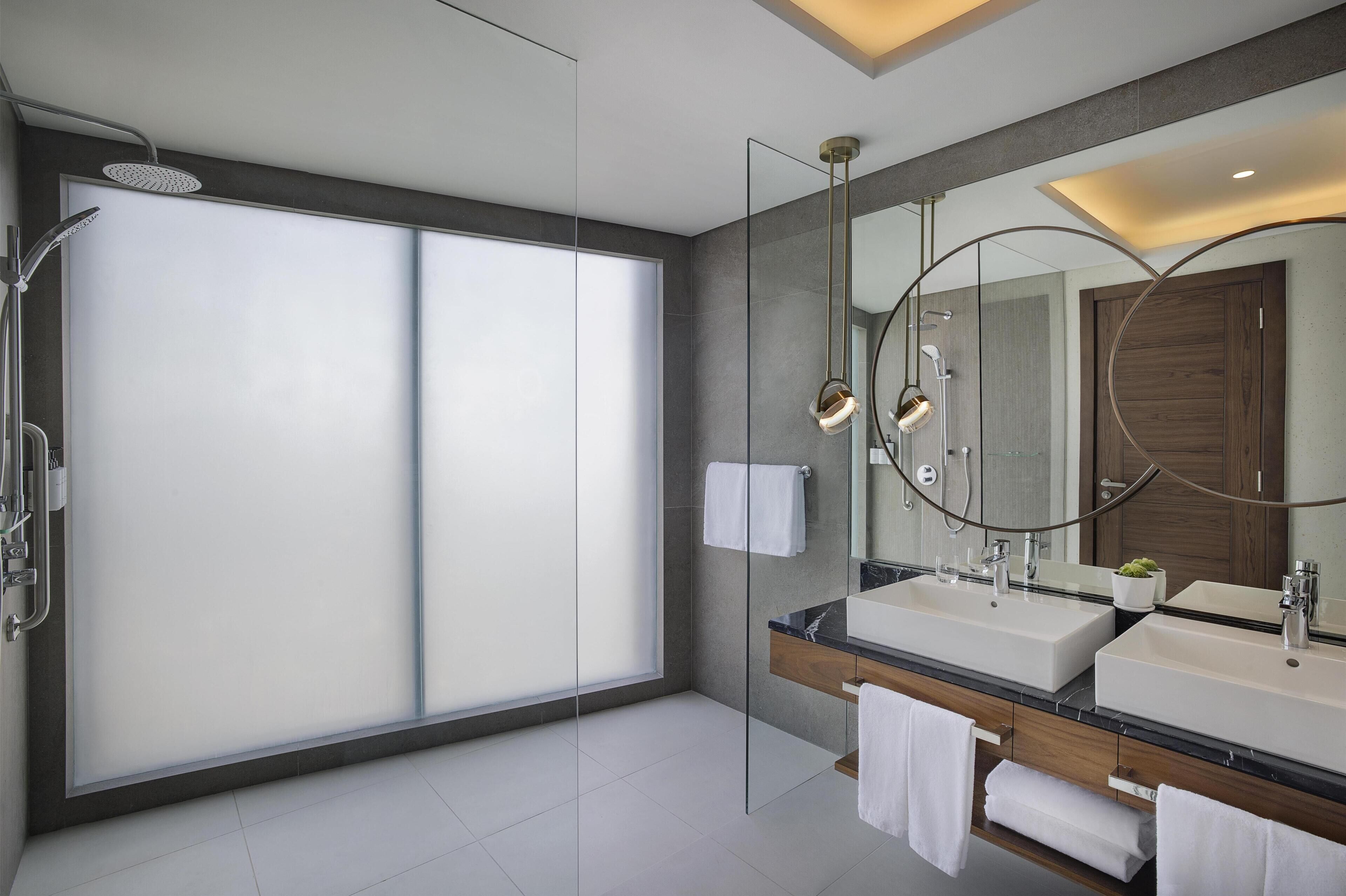 A modern bathroom with a large sliding glass door, two sinks, a mirror, and a shower.