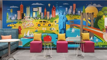 Ein Zimmer mit Wandgemälde von New Yorker Wahrzeichen, einem blauen Sofa, einem kleinen runden Tisch und zwei rosafarbenen Poufs.