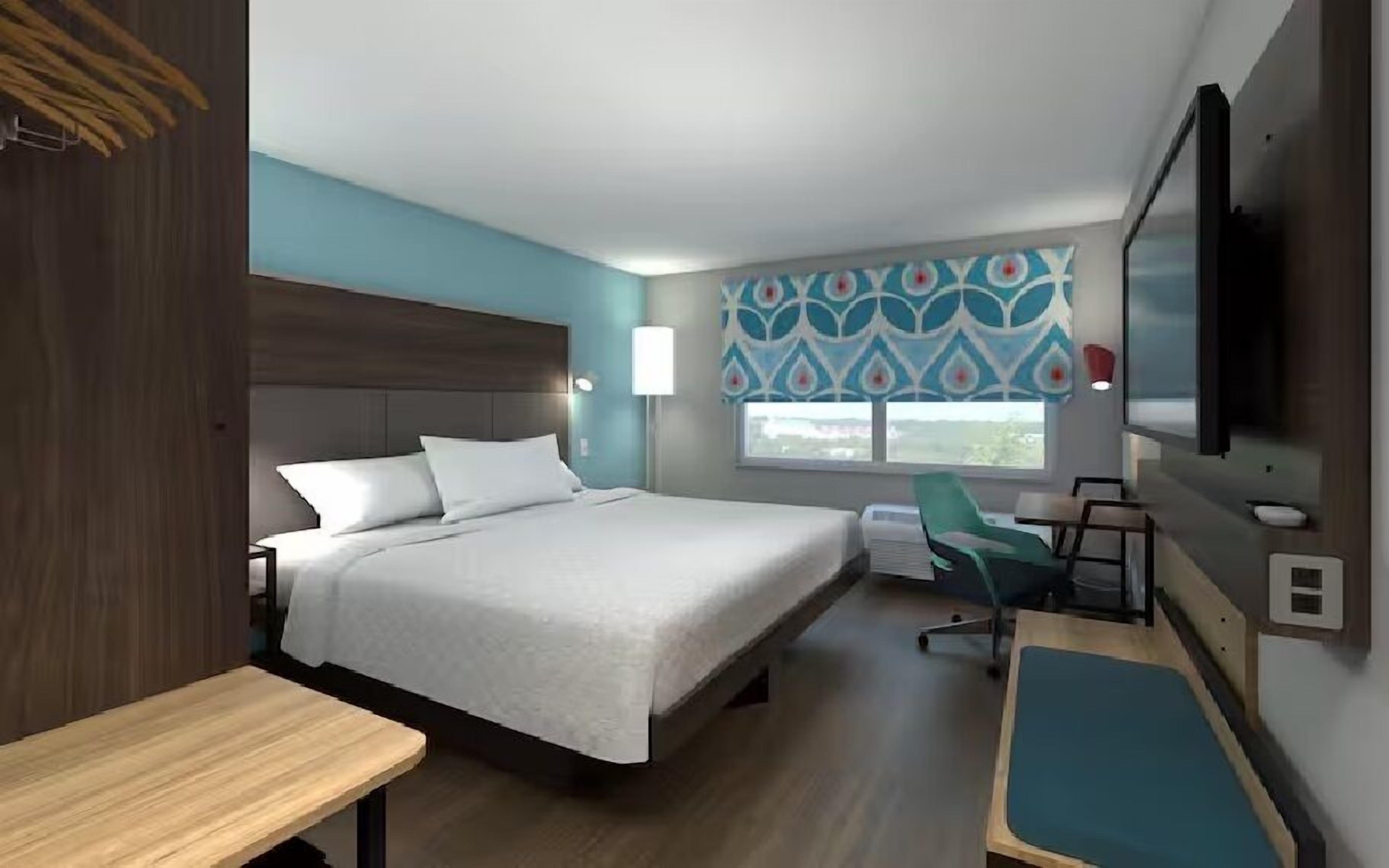 Habitación de hotel con cama, escritorio, silla, televisor y ventana con vistas.