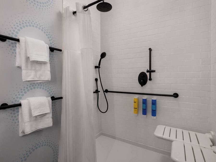 Un baño moderno con paredes de azulejos blancos, una ducha con pomo negro y un inodoro blanco.