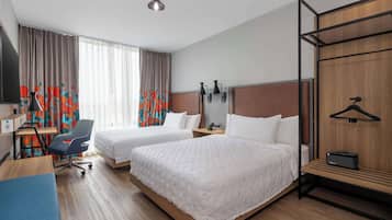 A hotel room with two beds, a desk with a chair, a TV, and a wardrobe with a hanging rack.