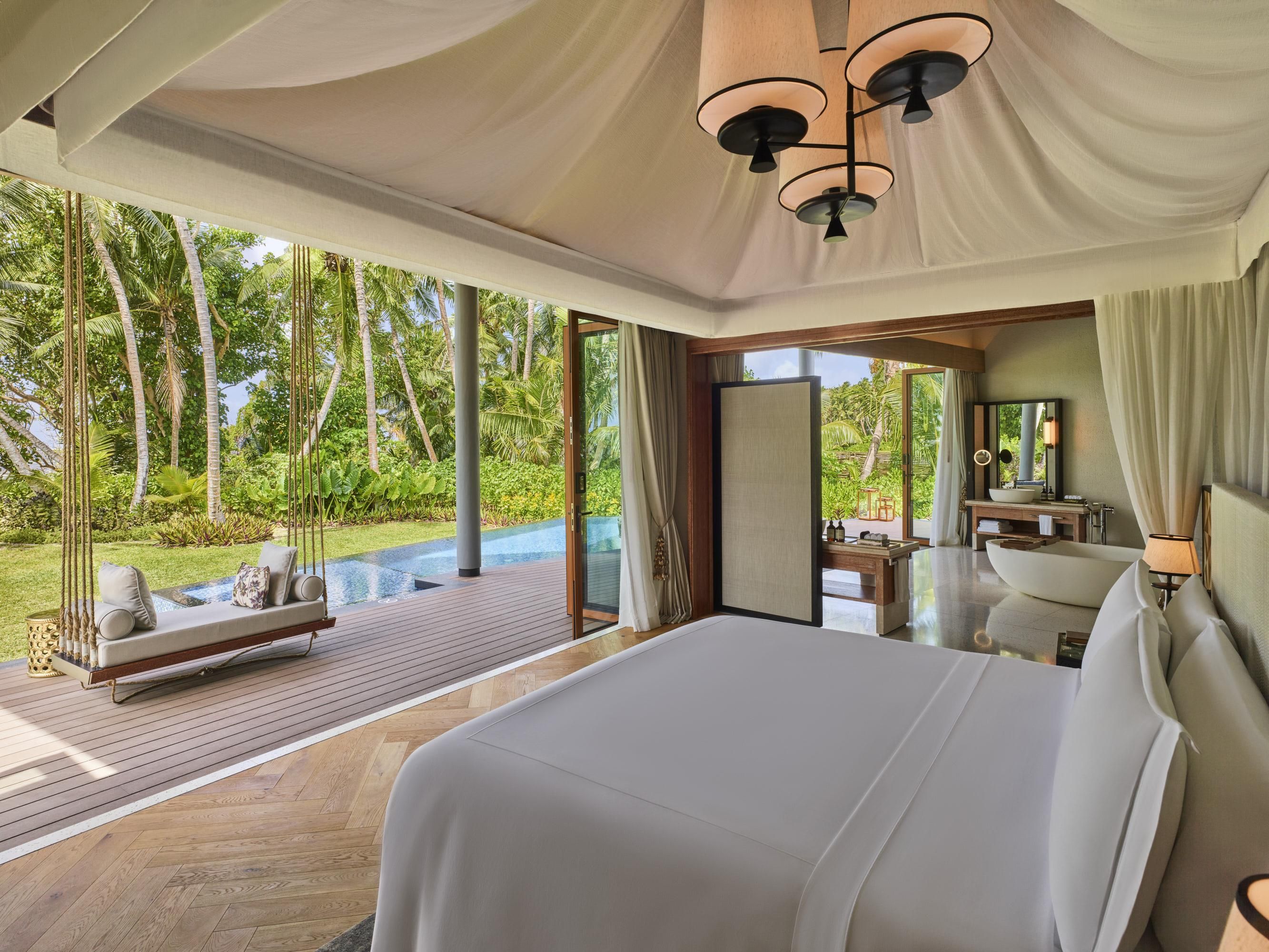 Quarto espaçoso com uma cama grande, um deck de madeira e vista para um verde exuberante.