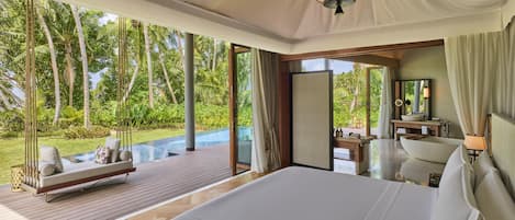 A spacious bedroom with a large bed, a wooden deck, and a view of lush greenery.