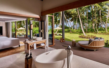 A modern bathroom with a freestanding bathtub, a wooden vanity, and a large window offering a view of a tropical garden and palm trees.