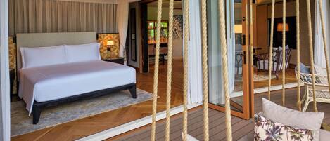 A hotel room with a large bed, a sitting area with a sofa and chairs, and a view of the outdoor area.