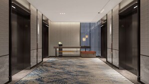 En moderne elevatorlobby med et mønstret tæppe, en bænk og en vægmonteret lampe.