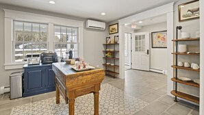 A kitchen with a wooden table, blue cabinets, and a microwave. There are shelves with dishes and a door with an exit sign. - Brook Bound Inn - Main Lodge - Deluxe King w/ Pullout Couch - Room 203
 (Wilmington)