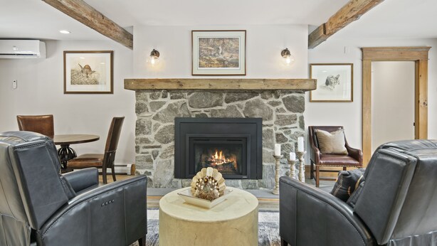 A cozy living room with a stone fireplace, leather chairs, and framed artwork on the walls. - Brook Bound Inn - Main Lodge - Deluxe King w/ Pullout Couch - Room 203
 (Wilmington)