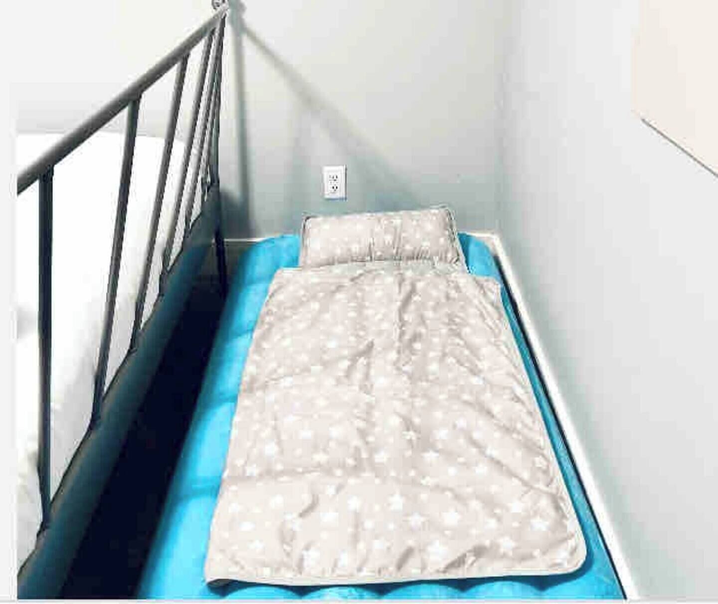 A small, single-bed room with a metal railing, a blue mattress, and a white wall with a power outlet.