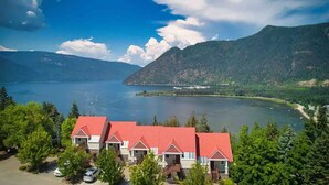 A lakeside property with multiple red-roofed buildings, surrounded by lush greenery and mountains.