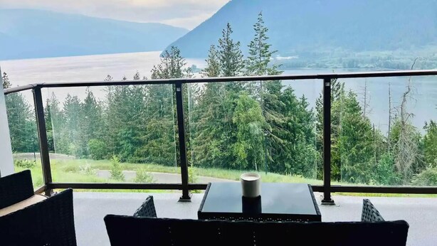 A balcony with a table and chairs, overlooking a lake and mountains.