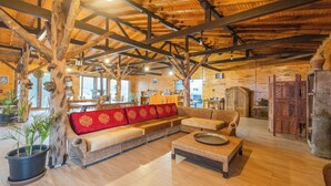 A rustic interior with a wooden ceiling, a sofa with red cushions, a wicker coffee table, and a large potted plant. - Kadir's Eco Life (Kumluca)