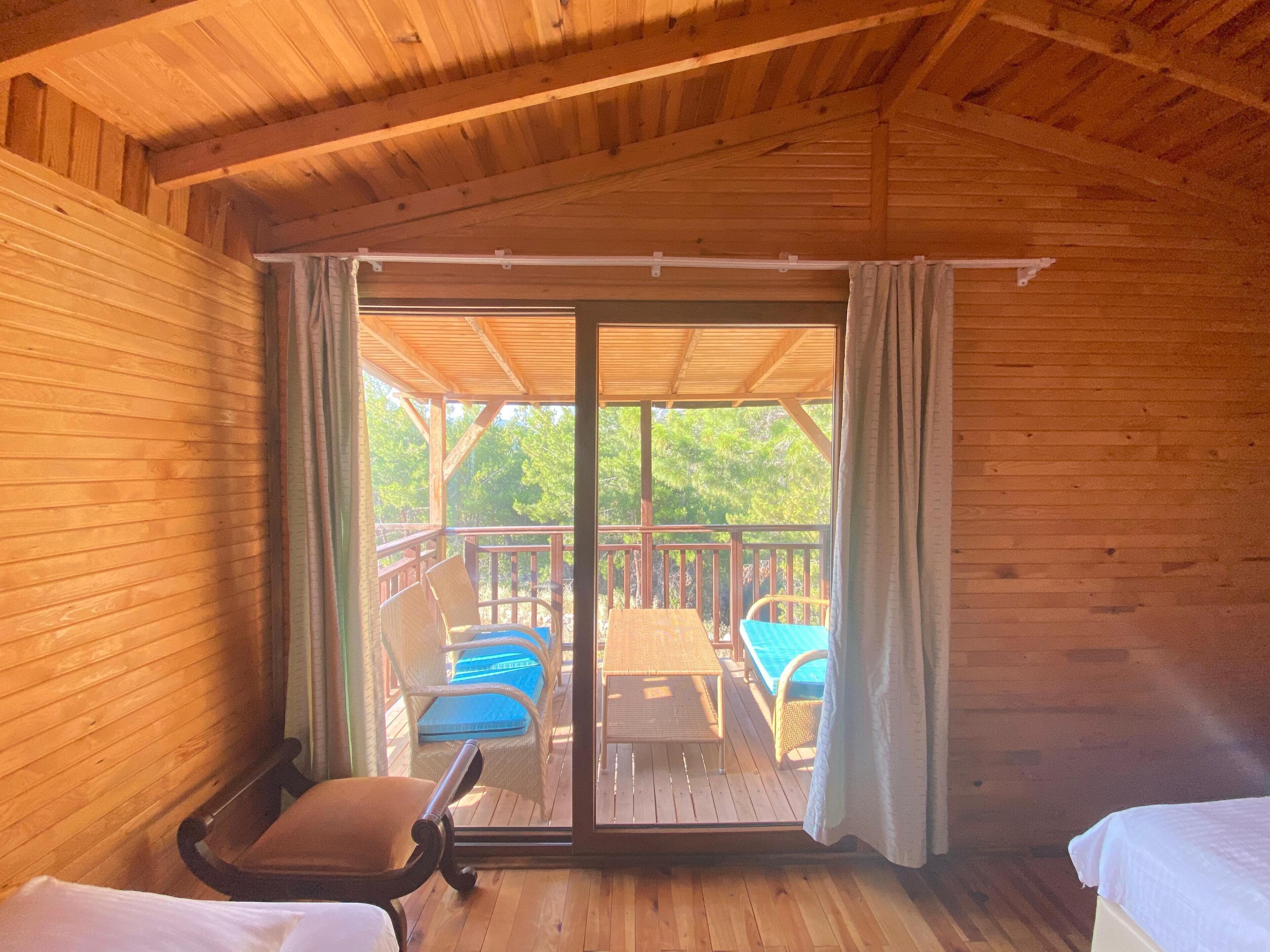 Een houten kamer met een schuifglasdeur die uitkomt op een terras met blauwe stoelen en een tafel.