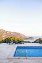 Piscina con sillas de descanso y vistas a las montañas y al mar.