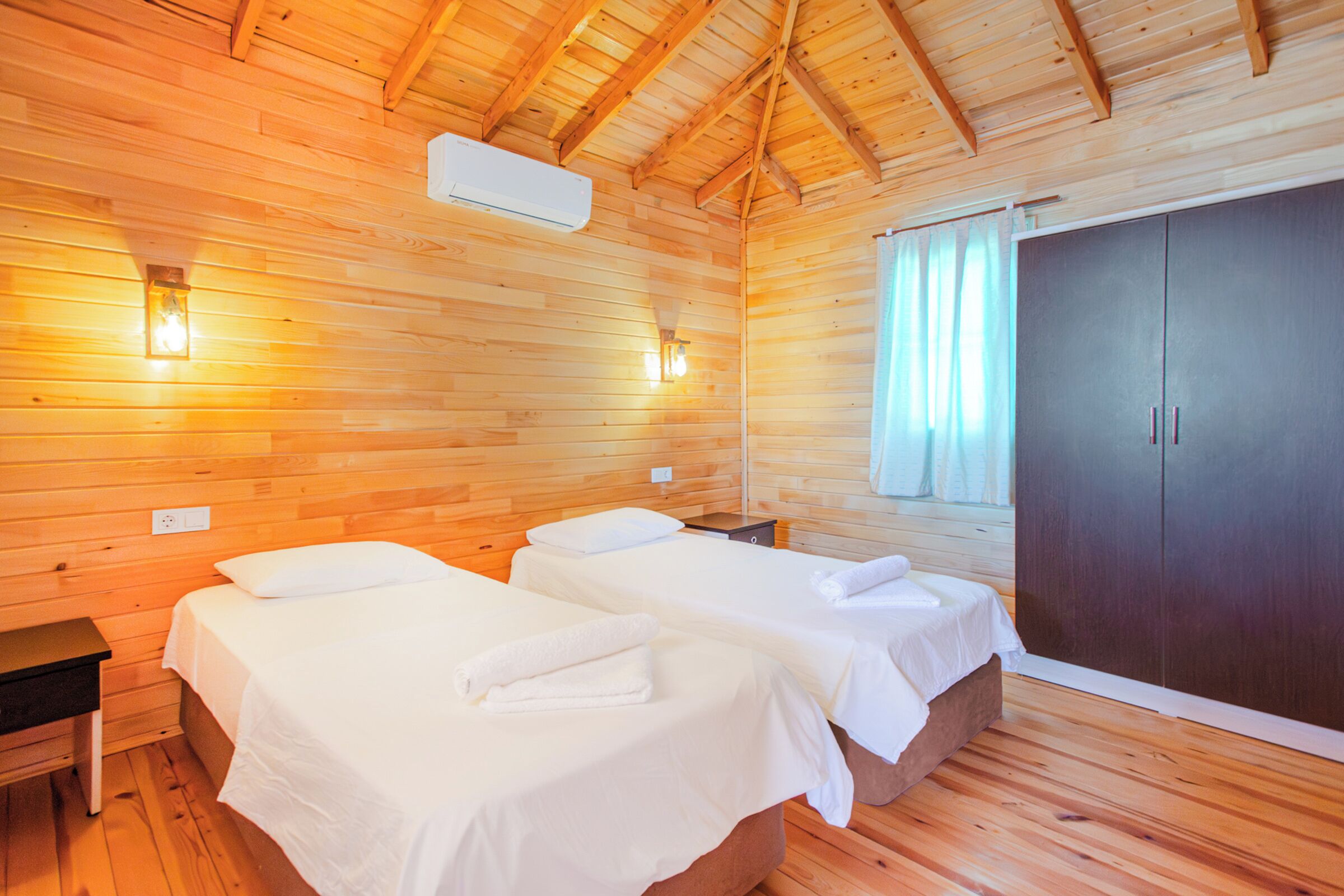 Una habitación de cabaña de madera con dos camas, un armario y una mesita de noche.