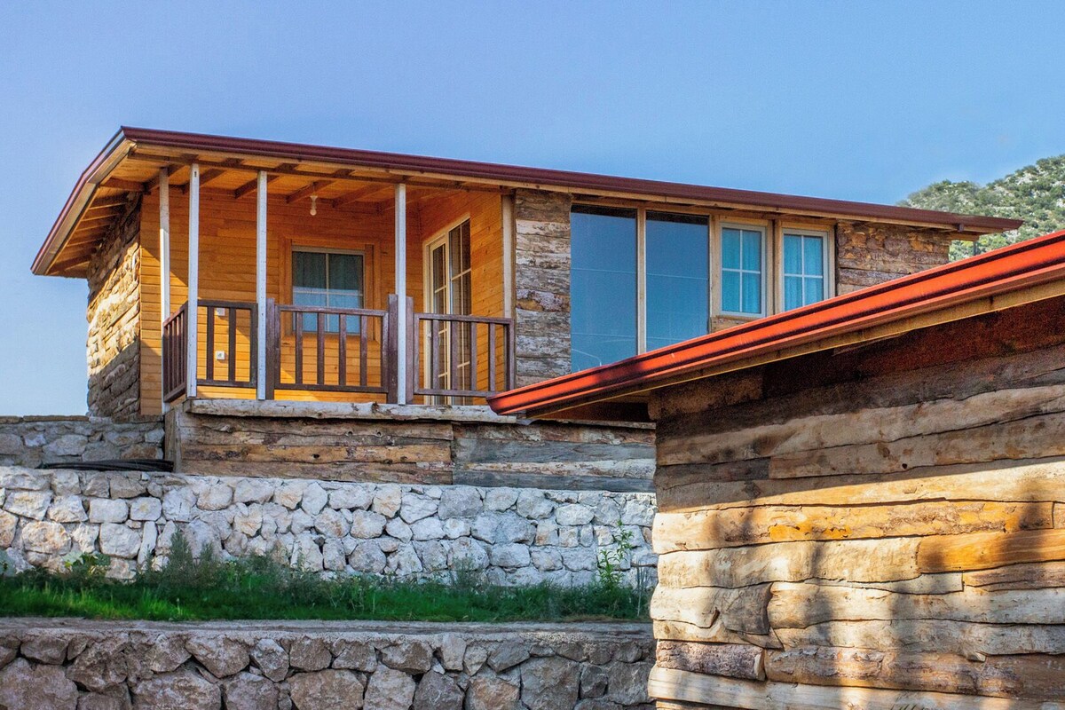 A log cabin with a stone foundation, a wooden porch, and large windows.