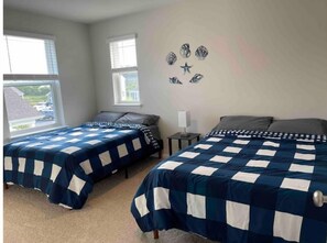Une chambre avec deux lits, chacun recouvert d’une couverture à carreaux bleus et blancs, une table de chevet avec une lampe, et une décoration murale représentant des étoiles et un poisson.