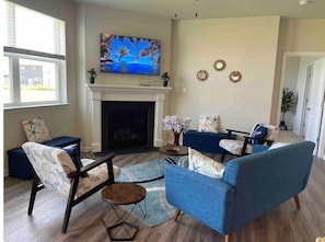 Un salon avec une cheminée, des canapés bleus et un téléviseur fixé au mur.