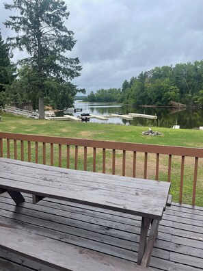 Eine Holzterrasse mit einer Bank, die auf einen ruhigen See mit angestaubten Booten blickt, umgeben von üppigem Grün.