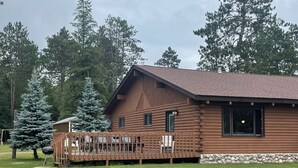 Eine Blockhütte mit einer Veranda, umgeben von einem grünen Rasen und hohen Bäumen.