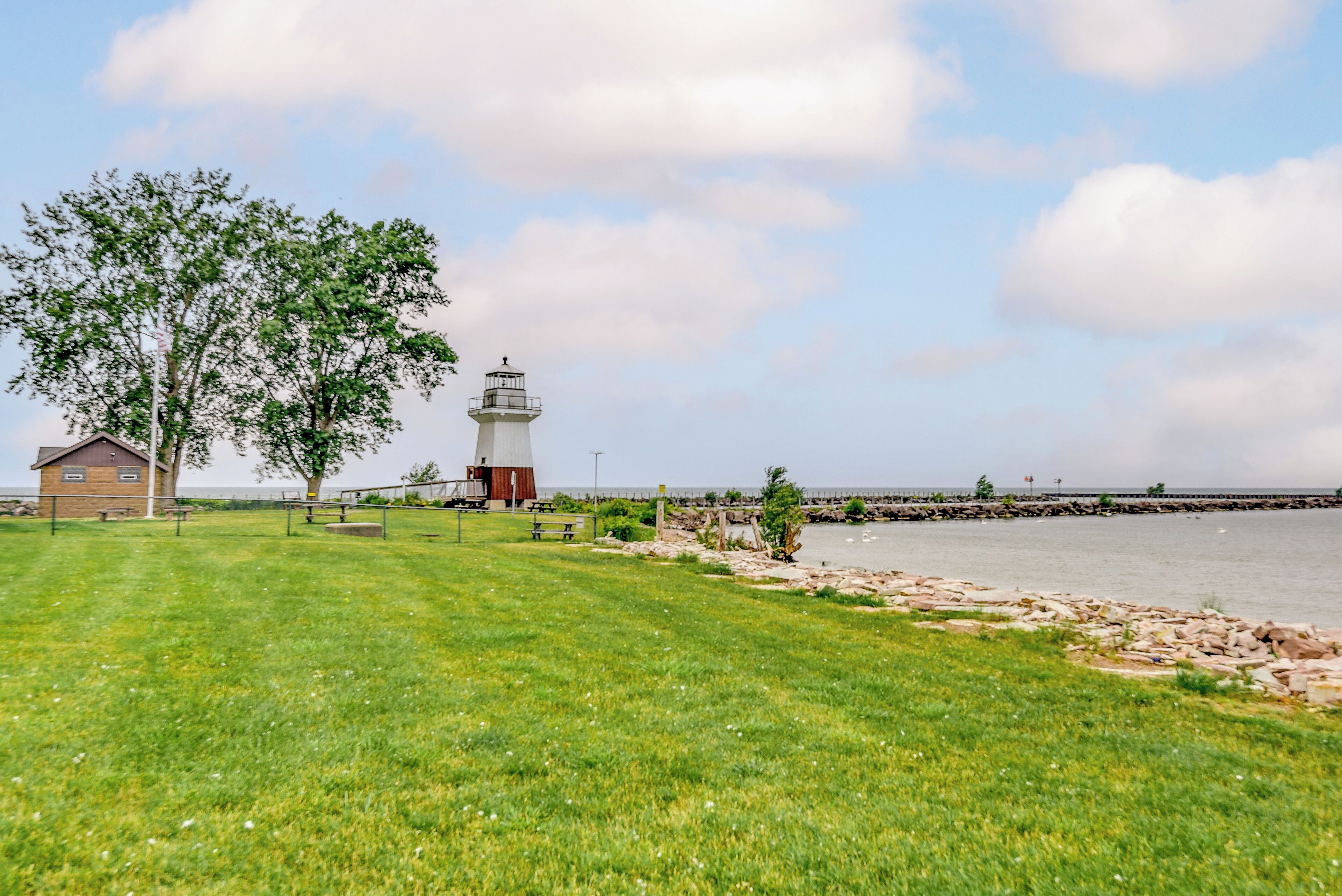 A grassy area with a lighthouse, a small building, and a rocky shoreline by the water.