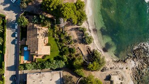 An aerial view of a coastal property with a swimming pool, a beach, and rocky terrain.