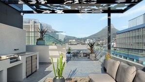 A rooftop terrace with a modern outdoor kitchen, seating area, and potted plants. - Designer Living at The Tokyo, No Loadshedding (Cape Town)