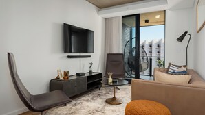 A modern living room with a sofa, a chair, a TV, and a small table. - Views and Luxury In Station House | No Loadshedding (Cape Town)