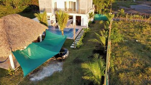 Una casa moderna con piscina, rodeada de exuberante vegetación y una estructura con techo de paja.