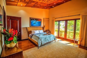 Quarto com cama, quadro, janela com cortinas e vista para o verde lá fora.