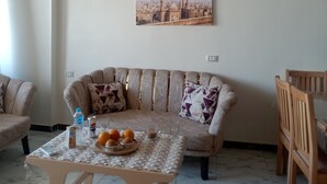 A living room with a sofa, a coffee table with oranges, a bottle of water, a can of Pepsi, and a glass of water. - Pyramids View apartment (Giza Governorate)