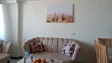 Un salon avec un canapé, une table basse sur laquelle se trouvent des oranges, une bouteille d’eau, une canette de Pepsi et un verre d’eau.