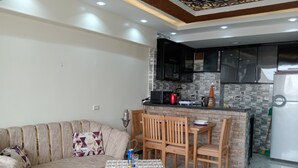 A living room with a sofa, a table with drinks, and a kitchen area with cabinets and appliances. - Pyramids View apartment (Giza Governorate)