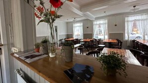 Een gezellig restaurant met houten tafels en stoelen, een toonbank met een menu, en een vaas met bloemen.