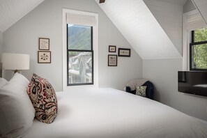 A bedroom with a large bed, a window with a view of a house, and a mounted TV. - The Residence on South Oak - downtown convenience! (Telluride)