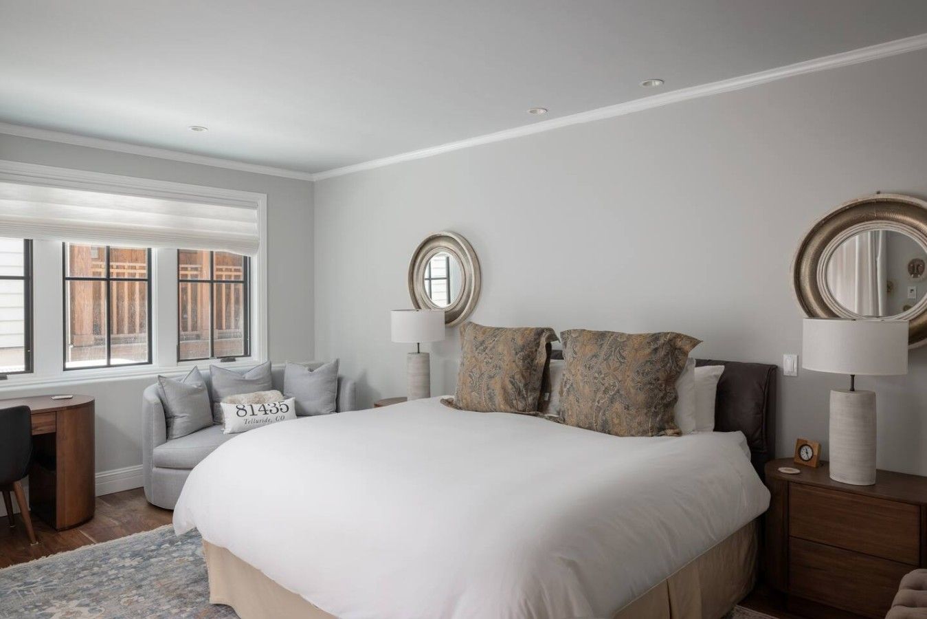 A bedroom with a large bed, two bedside lamps, a desk, and a chair.
