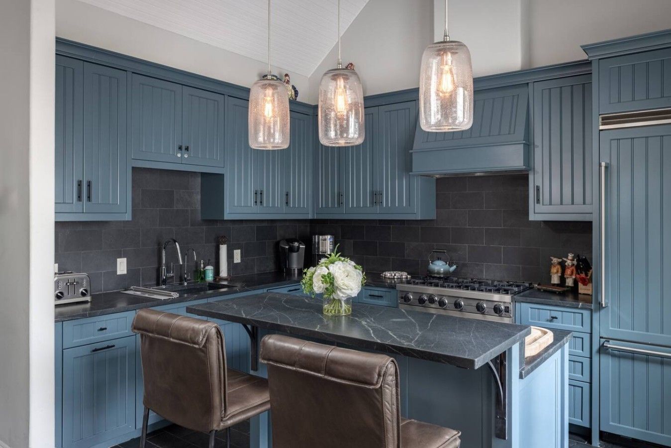 A kitchen with blue cabinets, a central island with chairs, and pendant lighting.