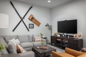 Un soggiorno moderno con un divano grigio, un tavolino, una TV e un mobile contenitore in legno scuro.