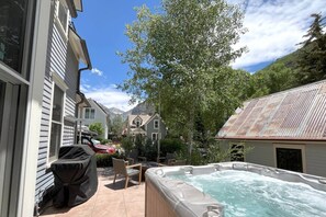 A backyard with a hot tub, a grill, and a patio table.