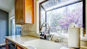 A kitchen with a large window, wooden cabinets, a stainless steel sink, and a marble countertop.