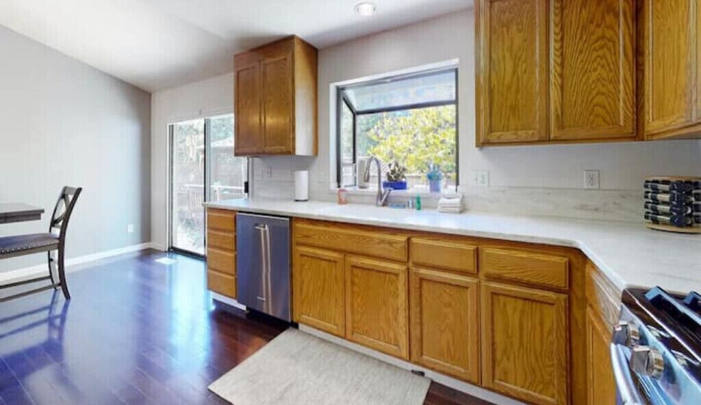 A modern kitchen with wooden cabinets, a built-in oven, and a window providing natural light.