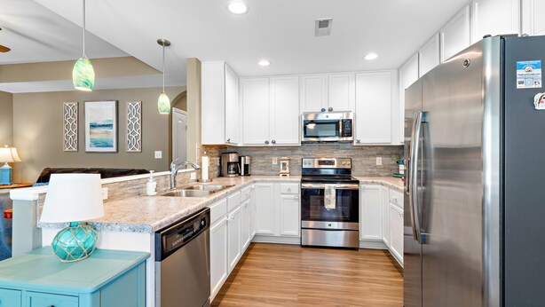 A modern kitchen with white cabinets, stainless steel appliances, and a wooden floor. - Sands About Right
 (Oak Island)