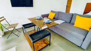 Ein modernes Wohnzimmer mit einem grauen Sofa, gelben Kissen, einem Holztisch und einem an der Wand befestigten Fernseher.