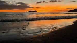Ein Strand mit Wellen bei Sonnenuntergang, eine entfernte Insel und ein klarer Himmel.