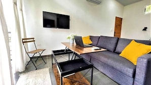 Ein modernes Wohnzimmer mit einem grauen Sofa, einem Holztisch, einem schwarzen Fernseher und einem Laptop.