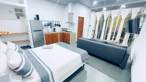 Et moderne hotelværelse med seng, sofa, tekøkken og et stort vindue med gardiner.